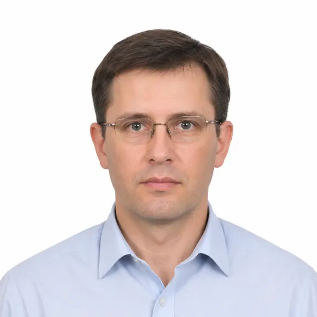 Passport-style portrait on white with the complete hair, shoulders, collar, and glasses visible.