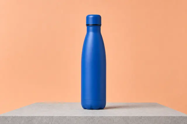 Matte cobalt-blue water bottle in a styled studio scene before background removal.